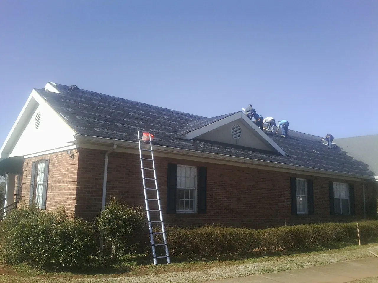 Crew tearing shingles off a brick ranch roof with a ladder set — Emergency Roof Repair work by our crew in Hutchinson