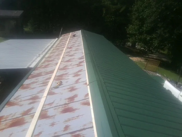 Old rusted panels beside newly installed green metal roofing — Wind Damage Roof Repair by Roofing Brothers in Hutchinson