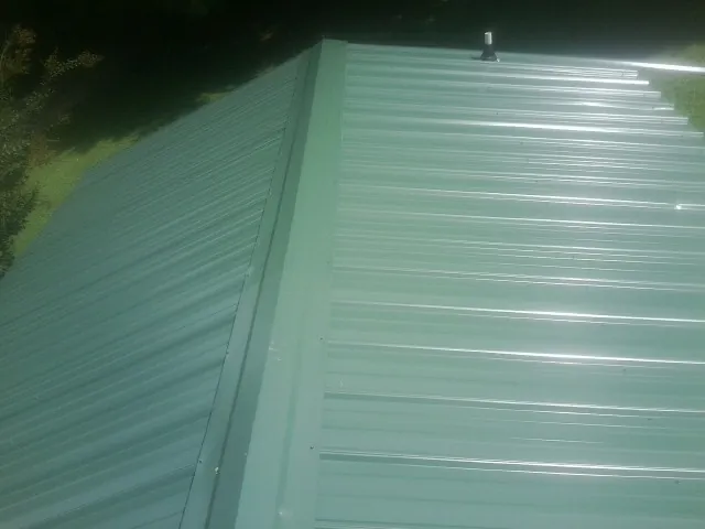 New green metal panels meeting at the ridge of a roof — Flat Roof Repair work by our crew in Hutchinson