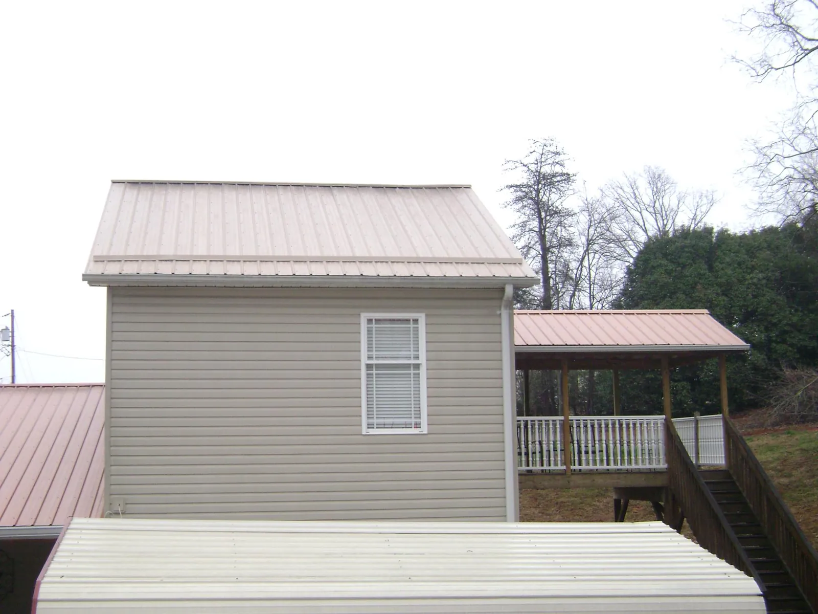 Tan metal roofs on a two story addition and attached porch, from a Roof Replacement job in Hutchinson