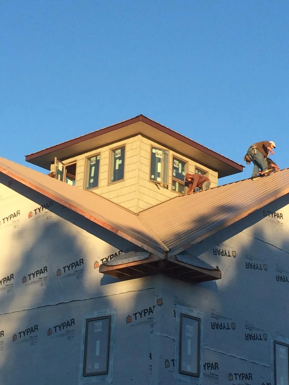 Roofers working around a rooftop cupola on a new metal roof at sunset — Roof Waterproofing in Hutchinson by Roofing Brothers